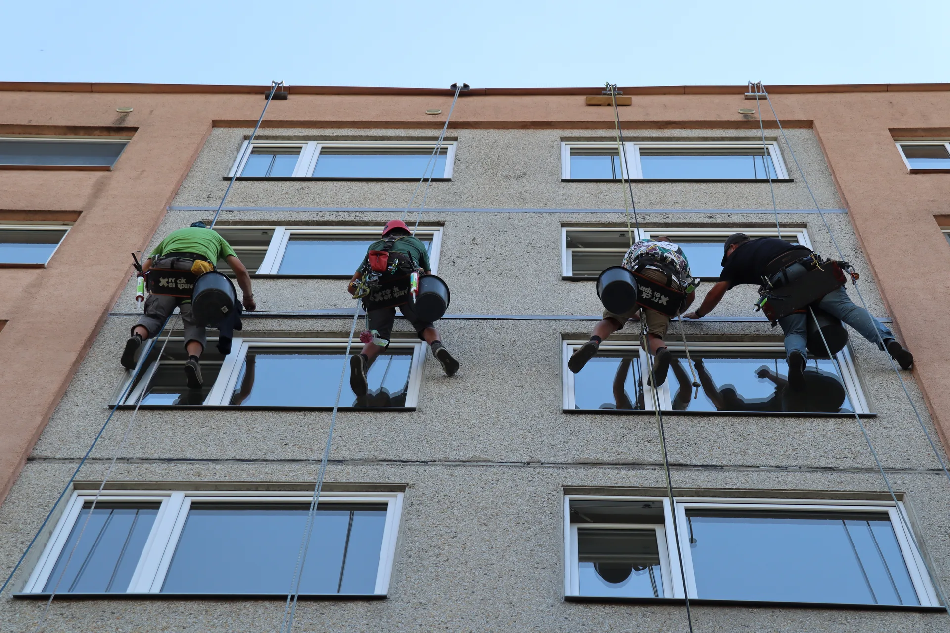 Tým výškových pracovníků na fasádě budovy